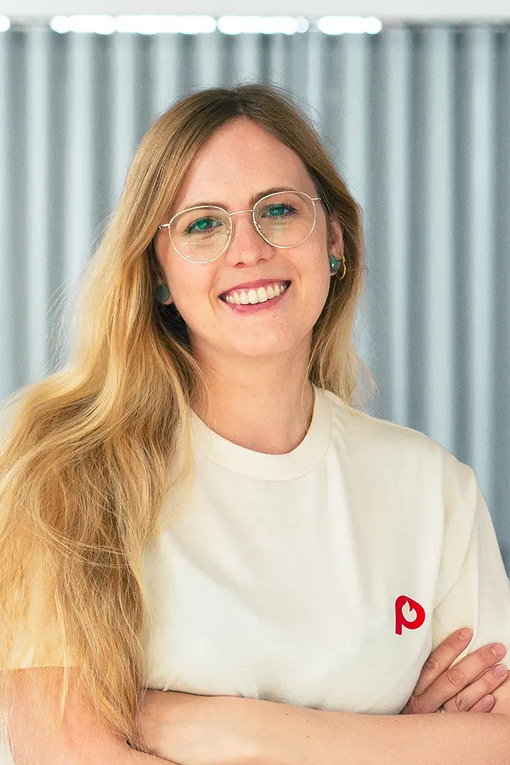 Portrait von Caro Schmid vom Pepper Pods Team mit beigem T-Shirt mit Pepper Pods Logo Submark vor unscharfem Hintergrund