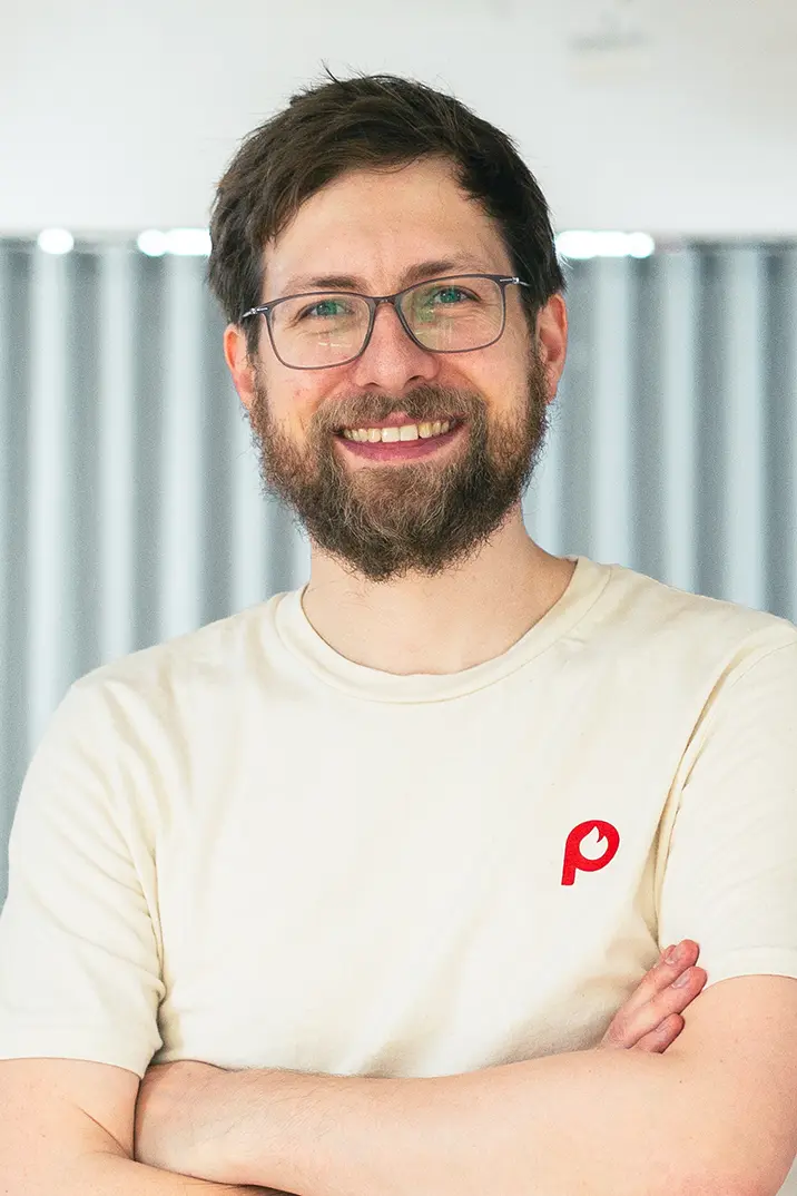 Portrait von Chris Schmid vom Pepper Pods Team mit beigem T-Shirt mit Pepper Pods Logo Submark vor unscharfem Hintergrund