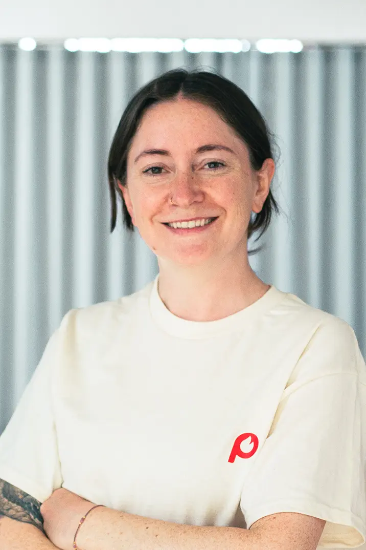 Portrait von Fini Meisl vom Pepper Pods Team mit beigem T-Shirt mit Pepper Pods Logo Submark vor unscharfem Hintergrund