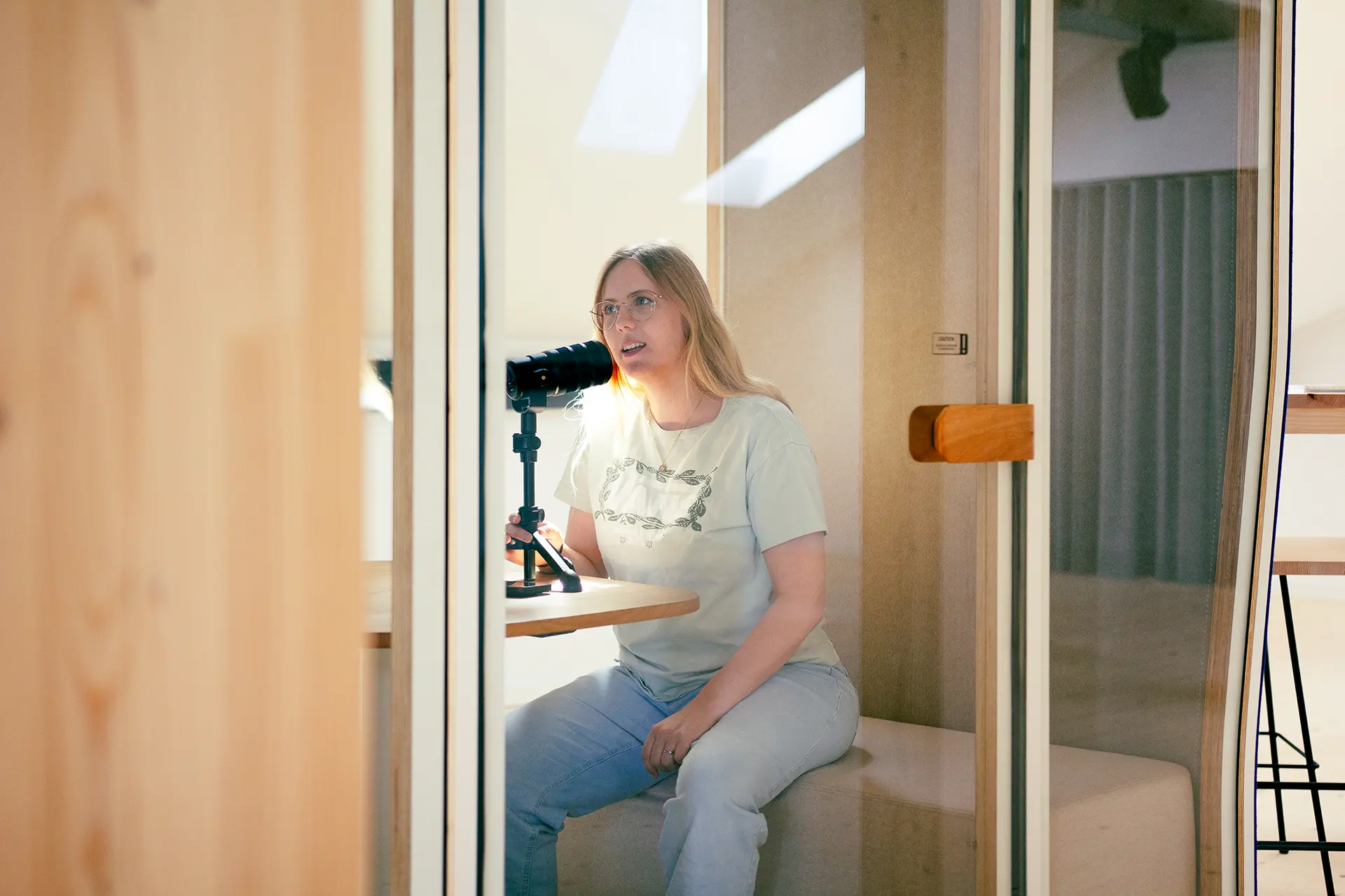 Im Tonstudio an einem auf dem Tisch stehenden Mikrophon sitzende Frau (Caro Schmid) bei der Tonaufnahme.