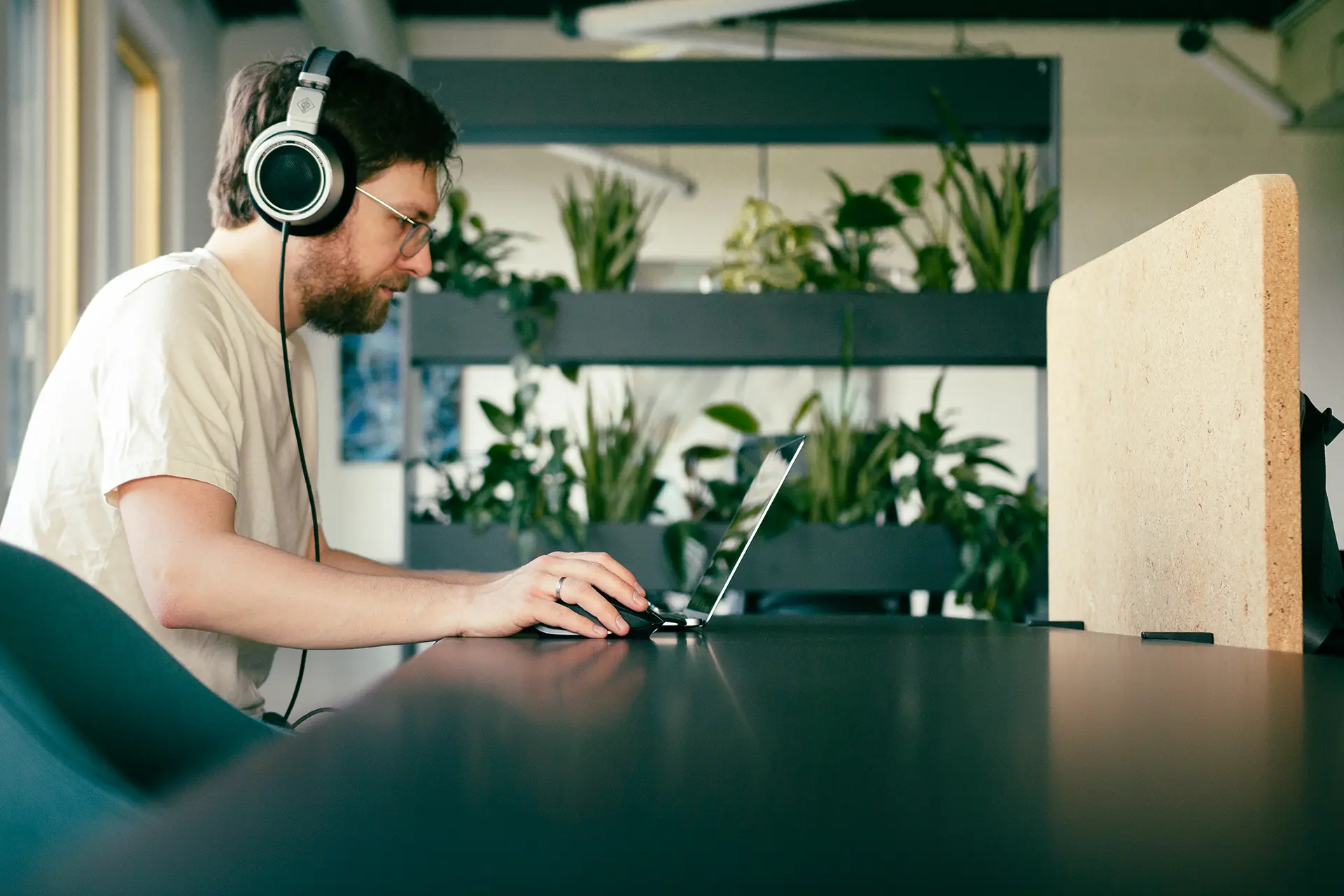 An einem Tisch sitzender Mann (Chris Schmid) mit Kopfhörern, Laptop und Maus beim Bearbeiten eines Podcasts.